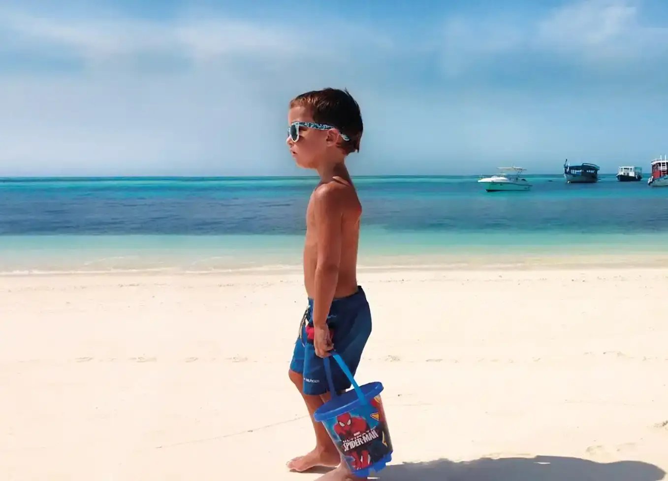 Kleiner Junge läuft mit einem Spiderman-Eimer am Strand am Meer entlang