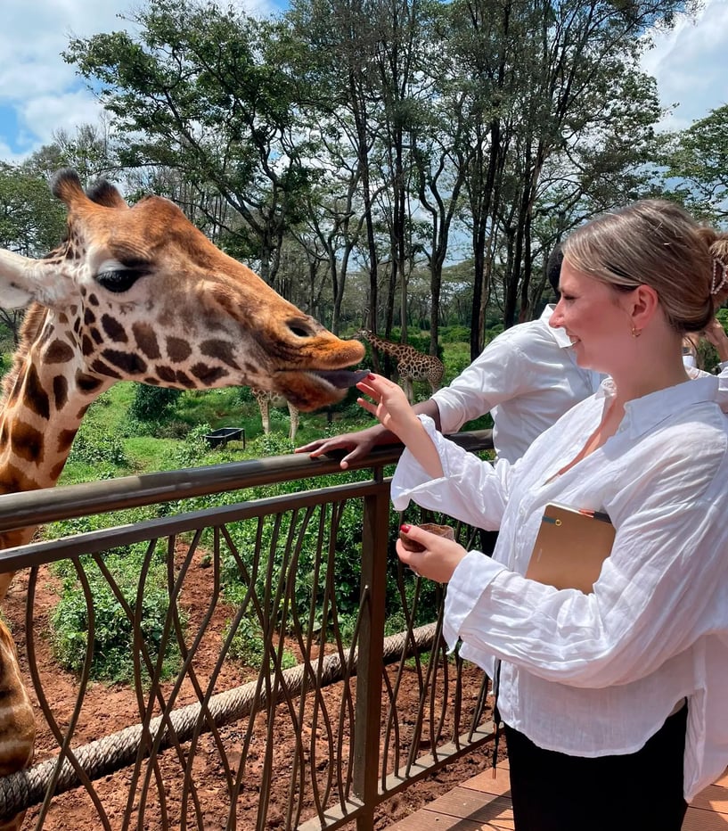 Isabella Arnold im Urlaub, steht auf einer erhöhten Plattform und füttert eine Giraffe