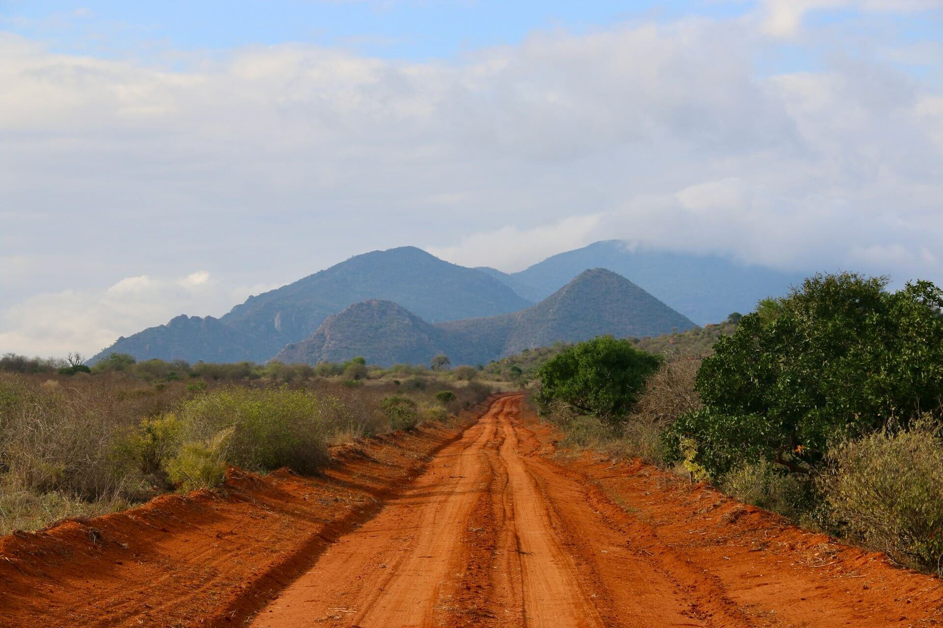 Straße aus der typisch roten Erde des Tsavo, im Hintergrund Berge.