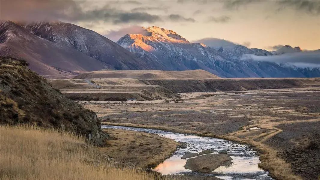 Brache Landschaft mit einem Fluss, im Hintergrund Berge