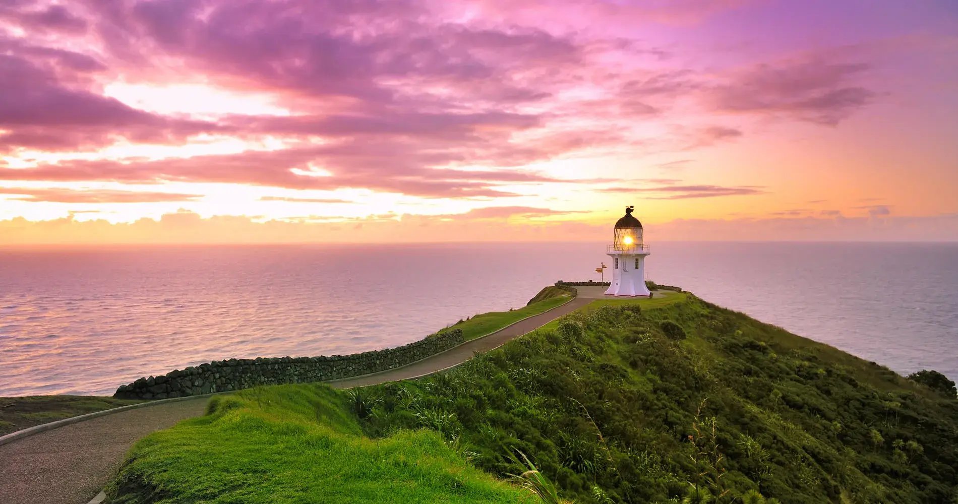 Leuchtturm auf einem grünen Hügel im Sonnenuntergang