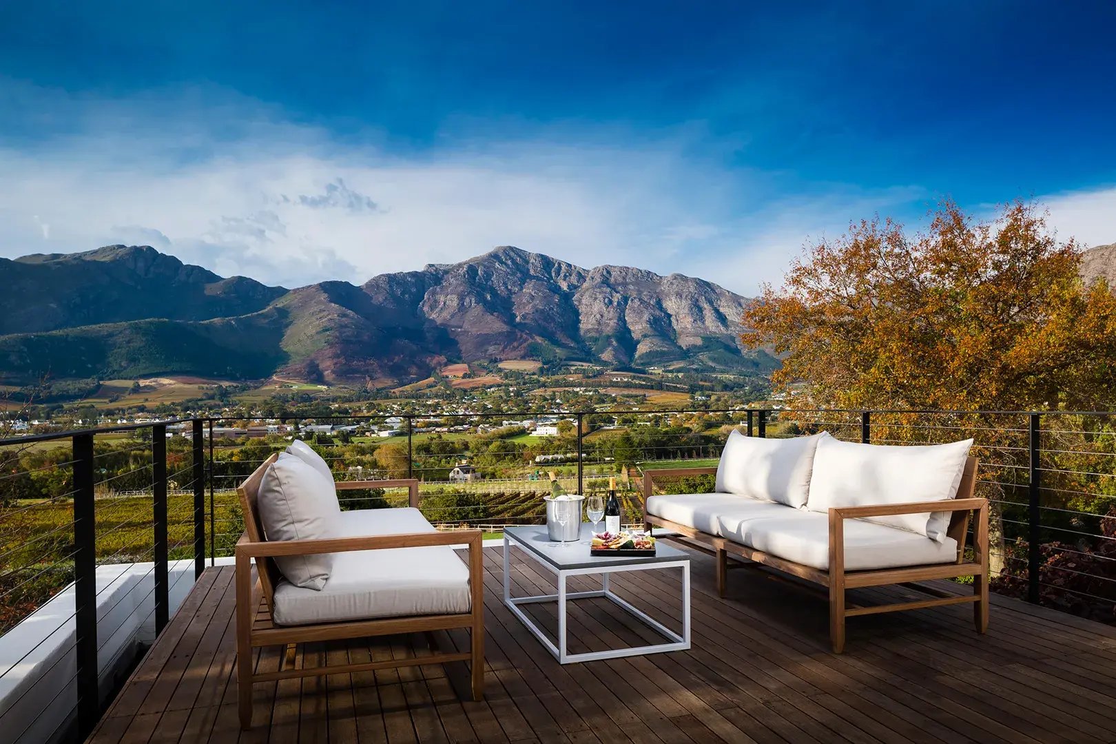 Auf einer Terrasse stehen weiße Sitzmöbel und ein Tisch mit Getränken. Im Hintergrund ist ein wunderschönes Bergpanorama.