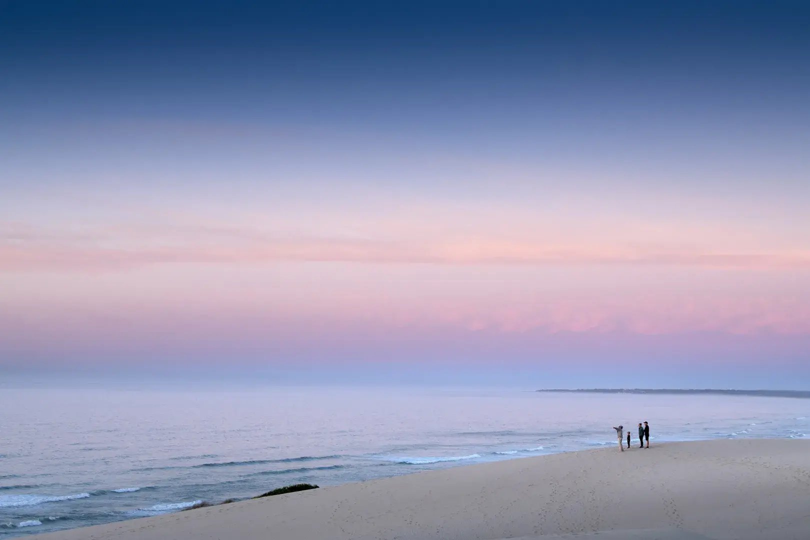 Zur Abendstunde steht eine Familie am endlosen Strand und blickt aufs Meer.