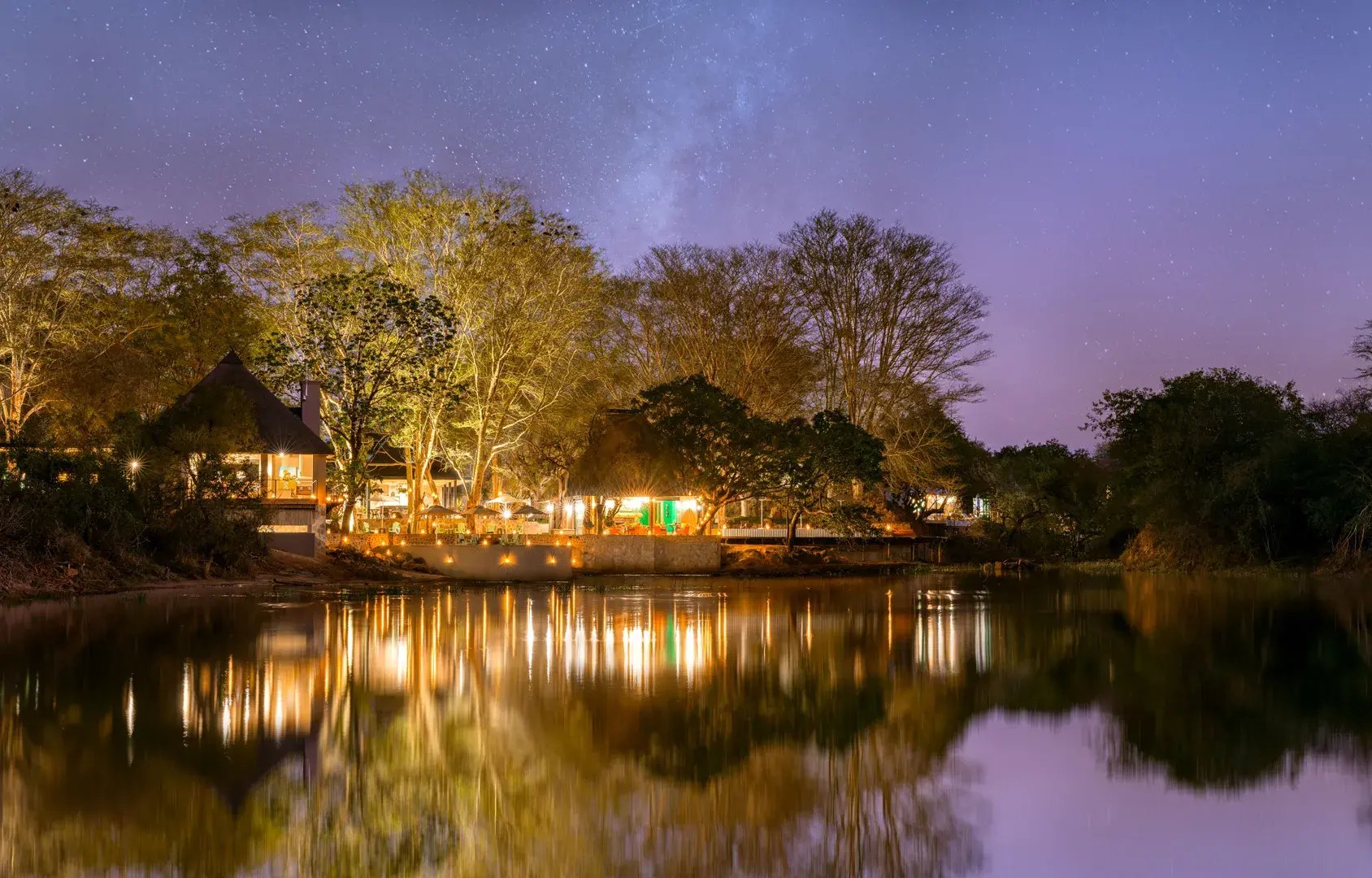 Blick vom Fluss auf die beleuchtete Lodge am Abend.