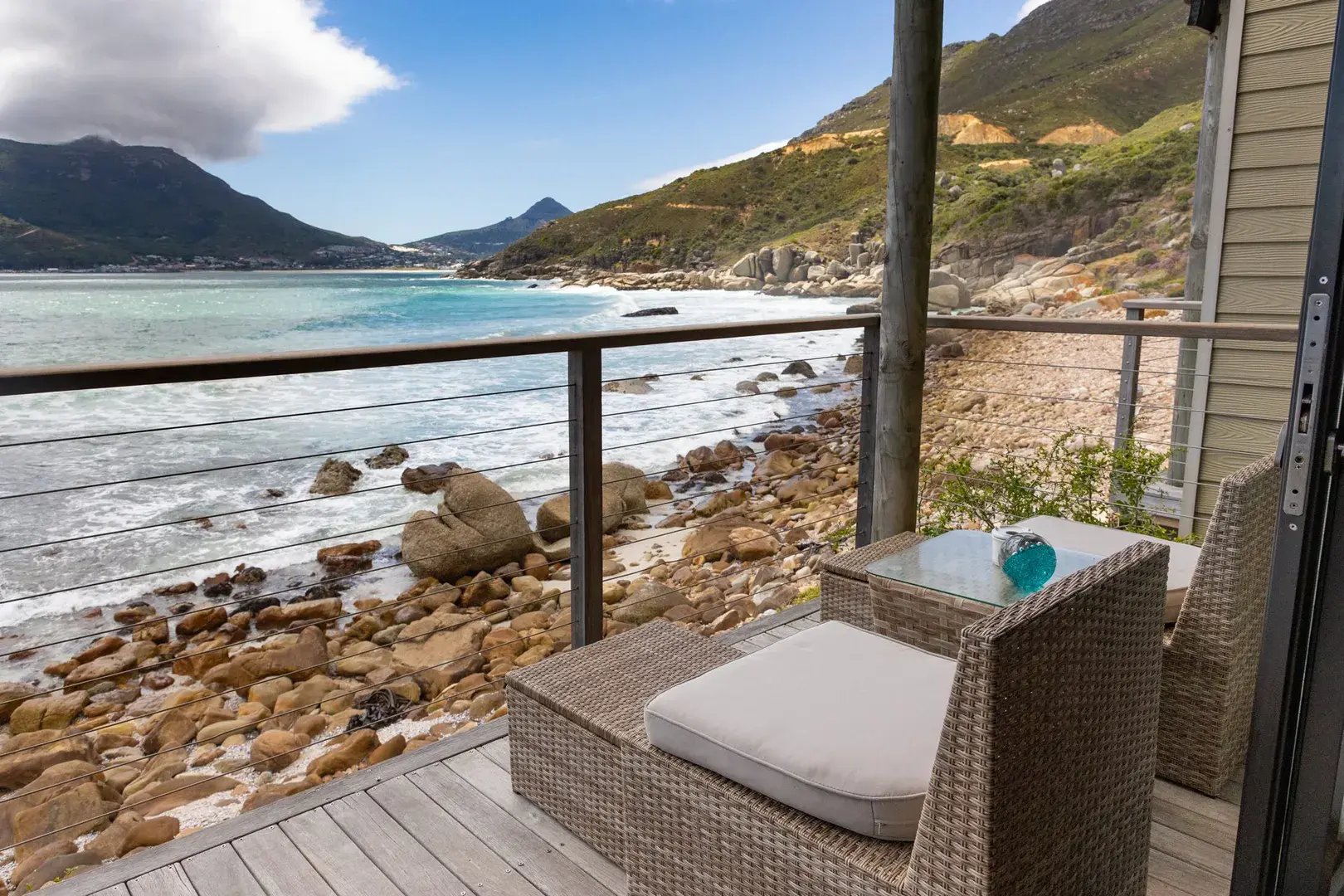 Auf einem Balkon stehen Rattanmöbel, die mit Blick auf das Meer ausgerichtet sind.