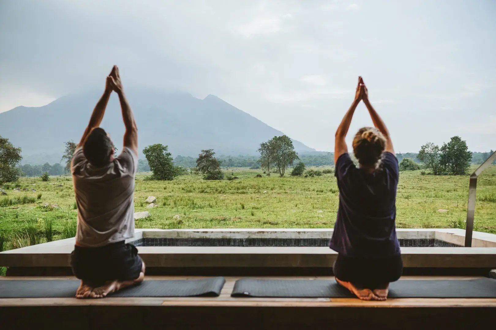 Ein Mann und eine Frau machen Yoga vor der grünen  Kulisse Ruandas.