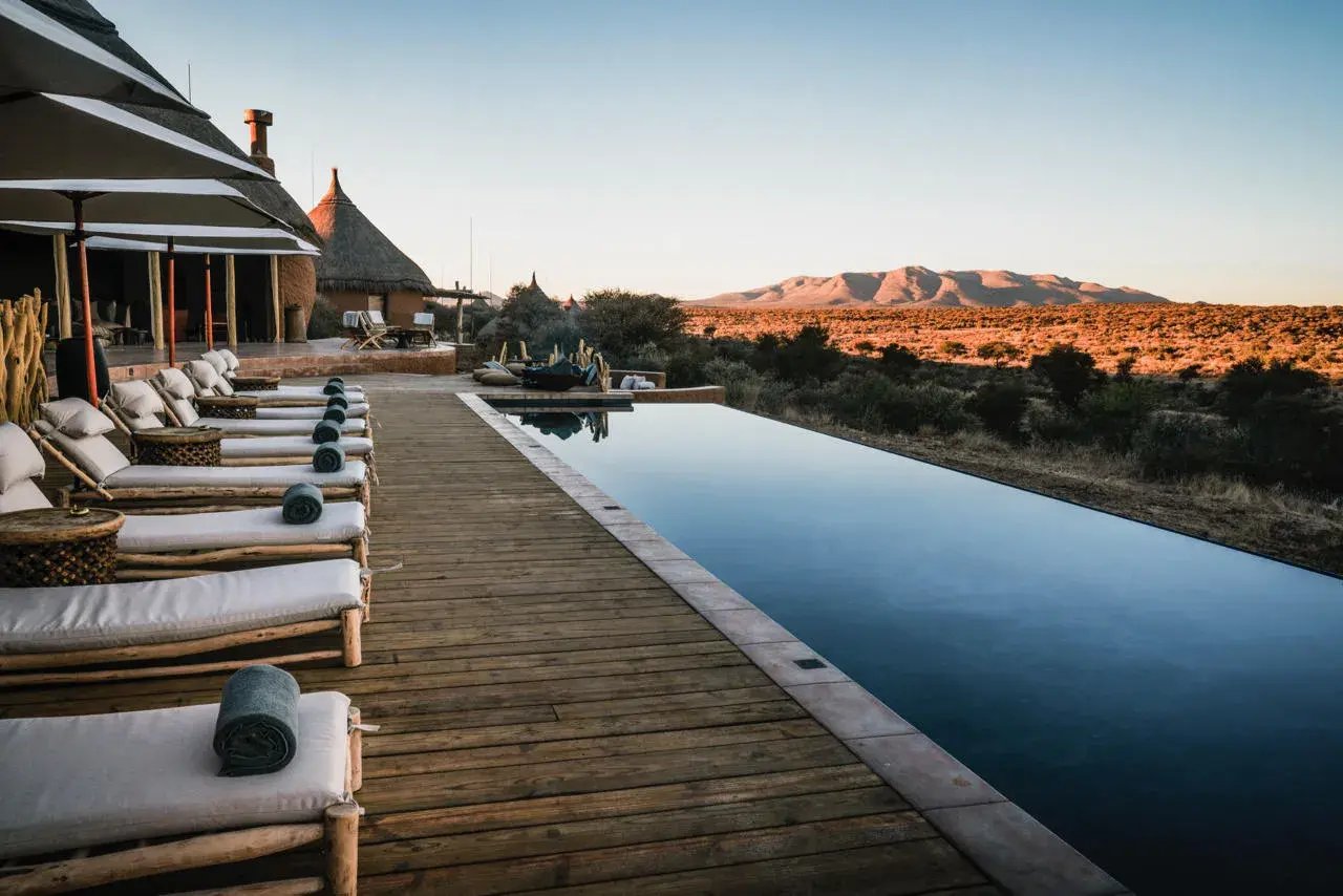 Infinitypool mit Sonnendeck und Blick auf die karge Landschaft Namibias.