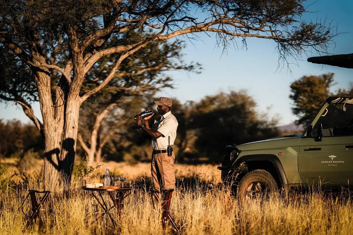 Ein Safariguide steht mit einem Fernglas in der Hand neben einem Jeep in der Wildnis.