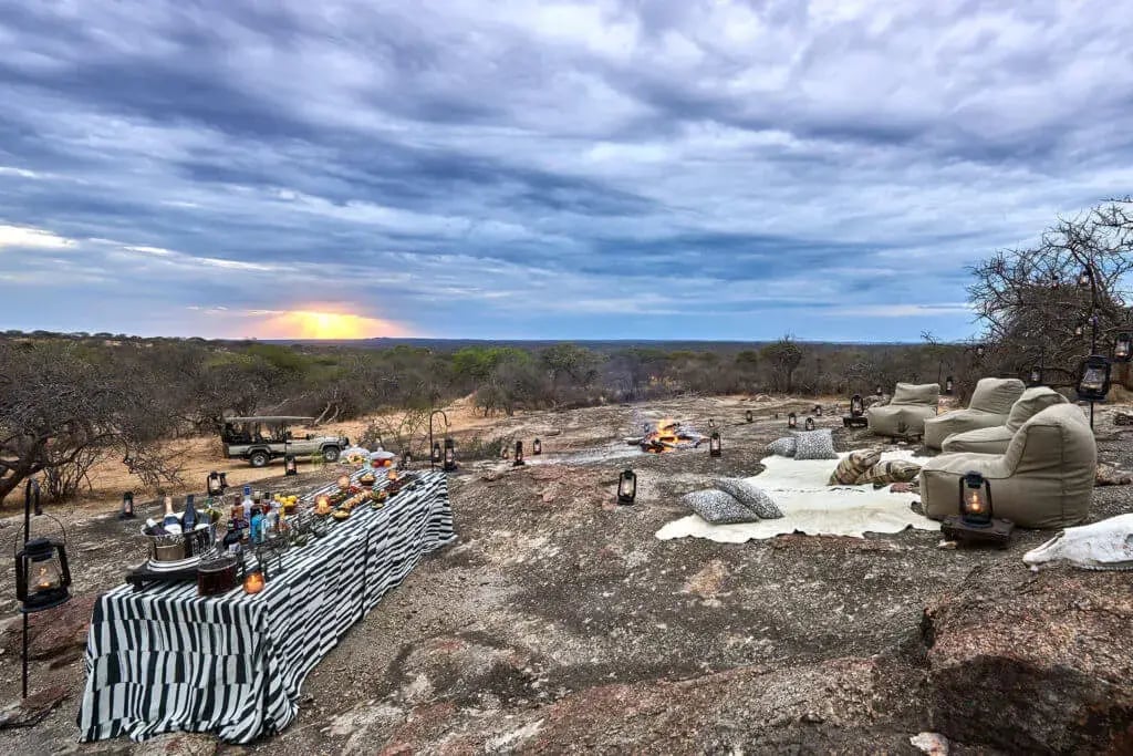 Auf einer großen Felsfläche wurden Sitzsätze, Decken, ein Lagerfeuer und Essen für einen Sundowner vorbereitet.