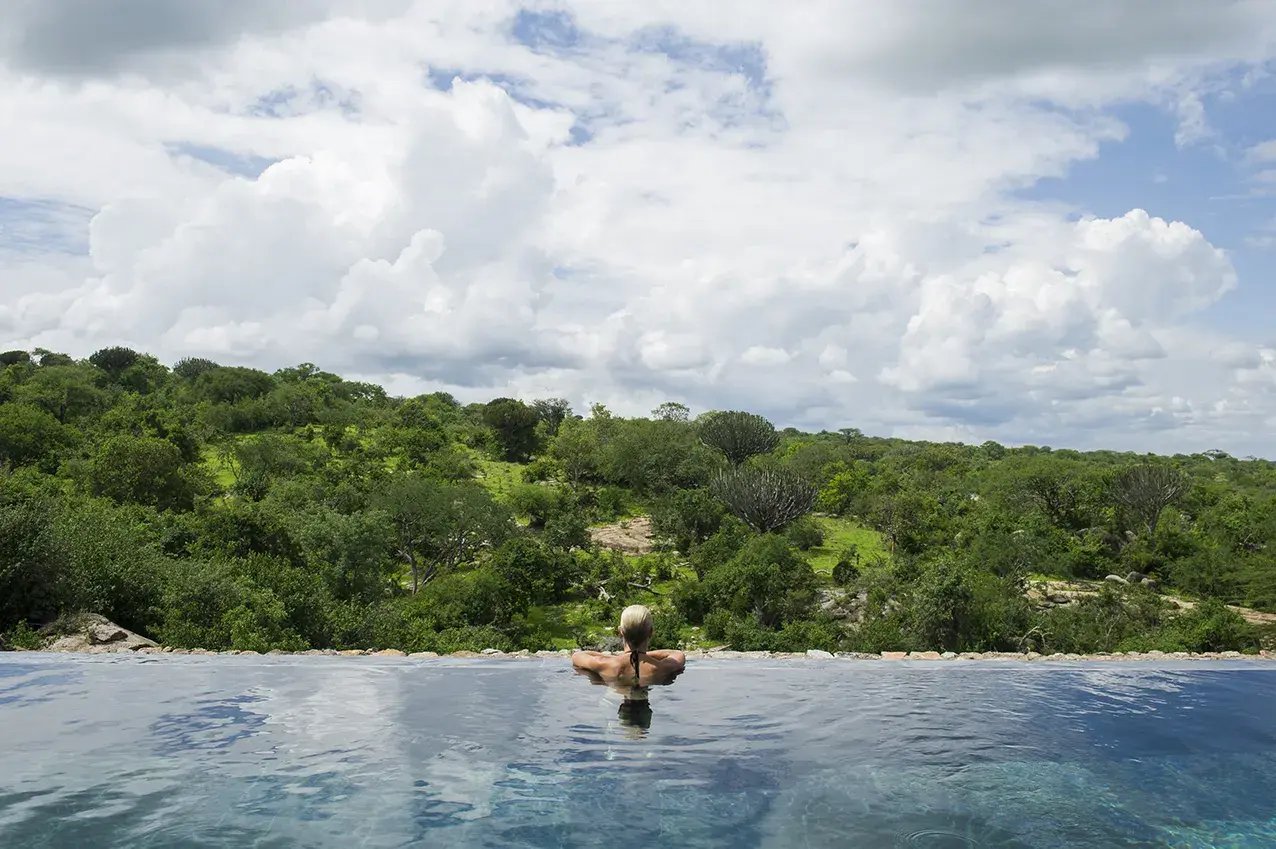 Eine Frau in einem Infinity-Pool blickt vom Rand in die grüne Landschaft.