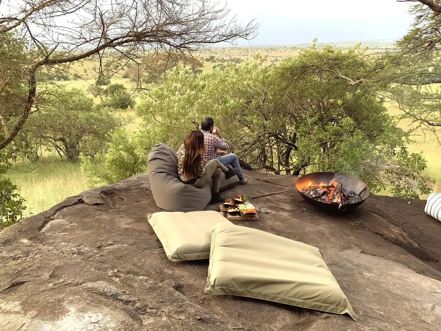 Ein Mann und eine Frau grillen auf einem Felsen und blicken in die Landschaft.