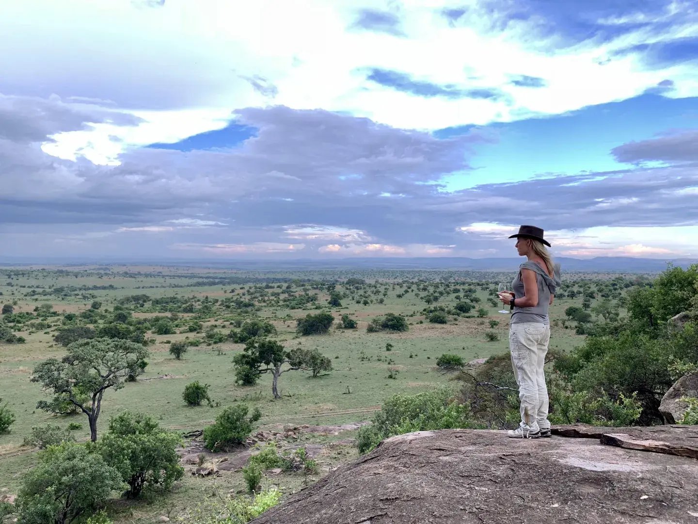 Eine Frau blickt mit einem Getränk in der Hand in die unendliche Weite der Serengeti.