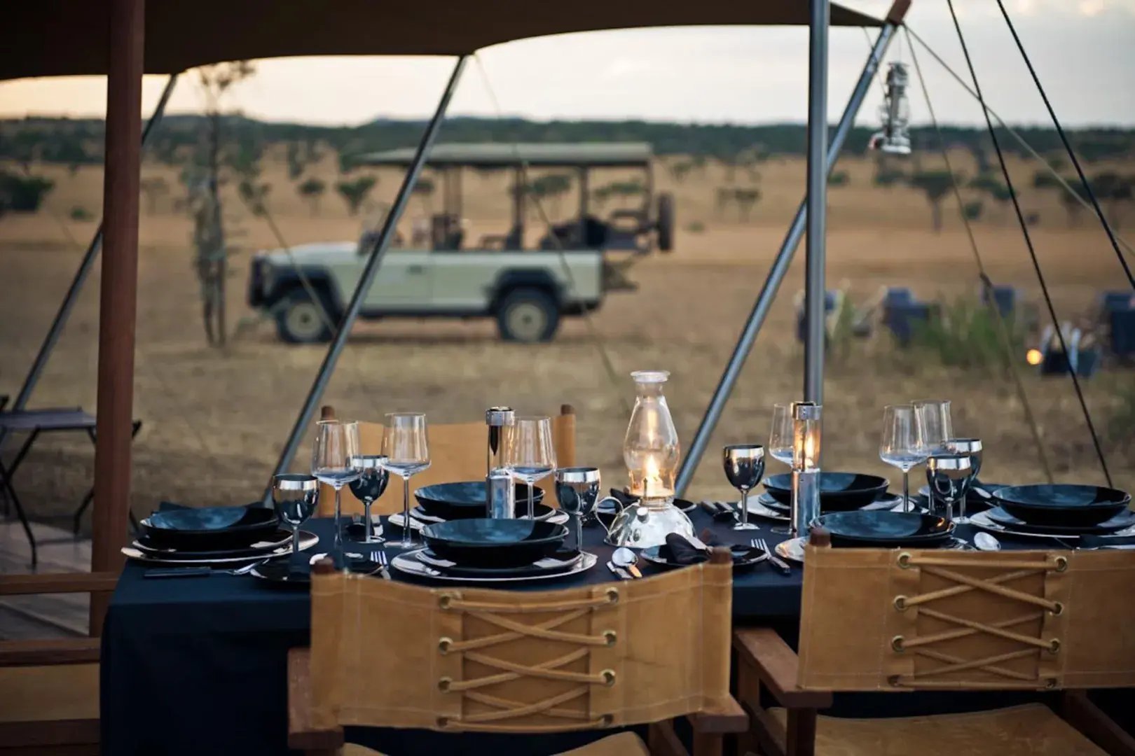 Safari-Dinner in der Wildnis, ein Jeep steht im Hintergrund.