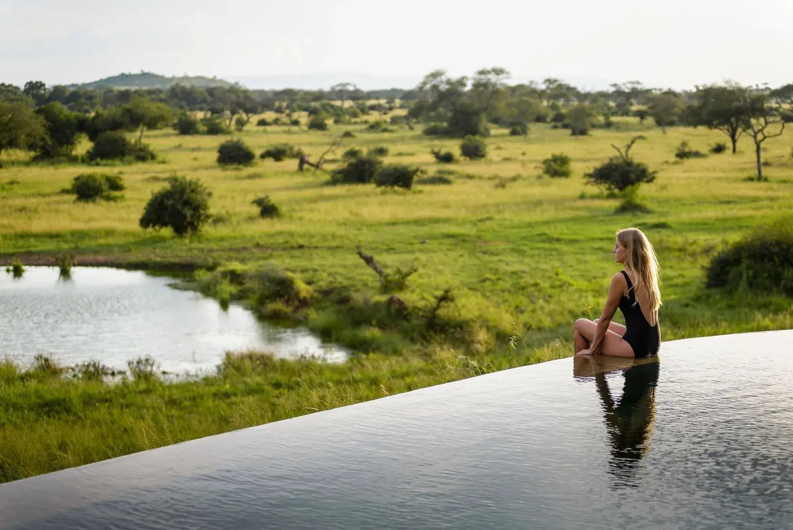 Eine Frau sitzt am Rand eines Infinity-Pools und blickt auf ein Wasserloch herab.