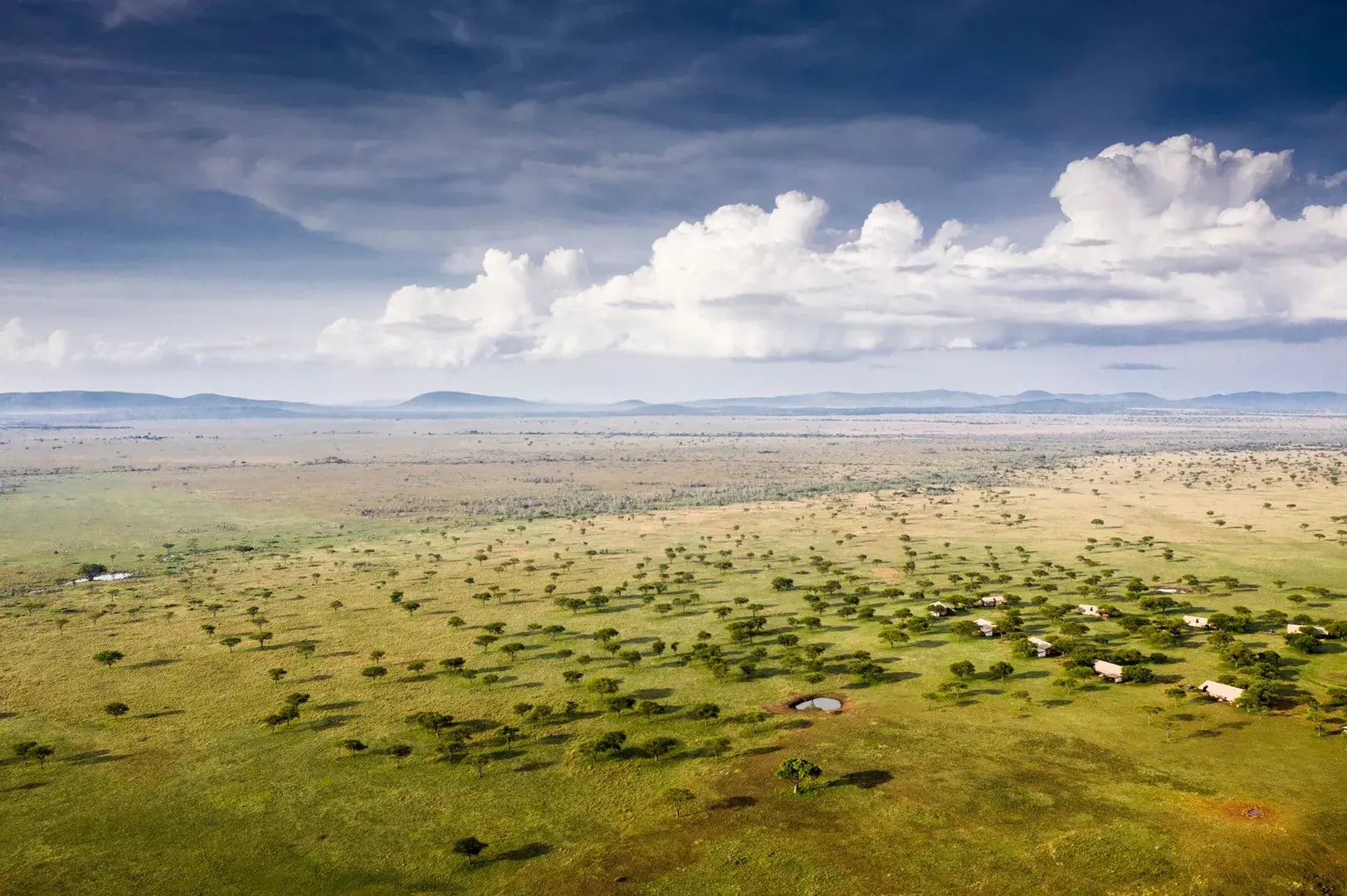 Luftaufnahme der Serengeti mit einem Camp, das ganz klein erscheint.