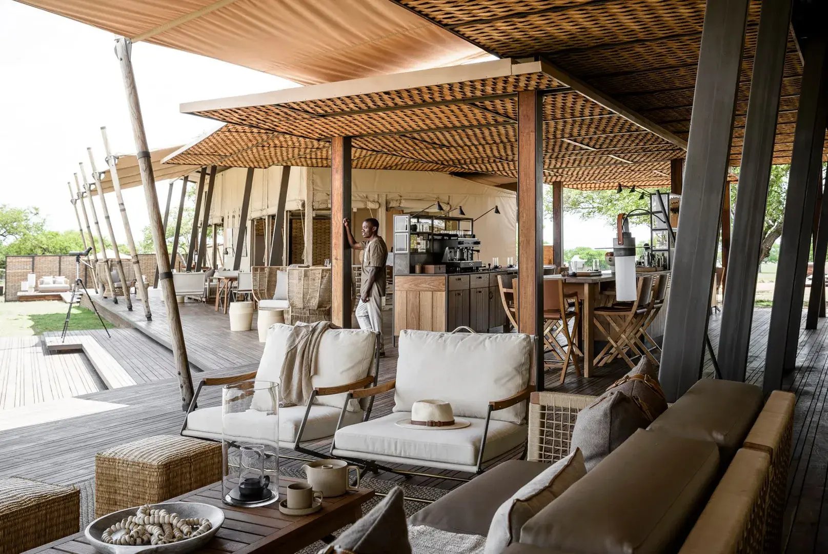 Große Terrasse mit gemütlichen Sitzmöbeln, ein Mann steht an einem Pfosten und blickt in die Ferne.