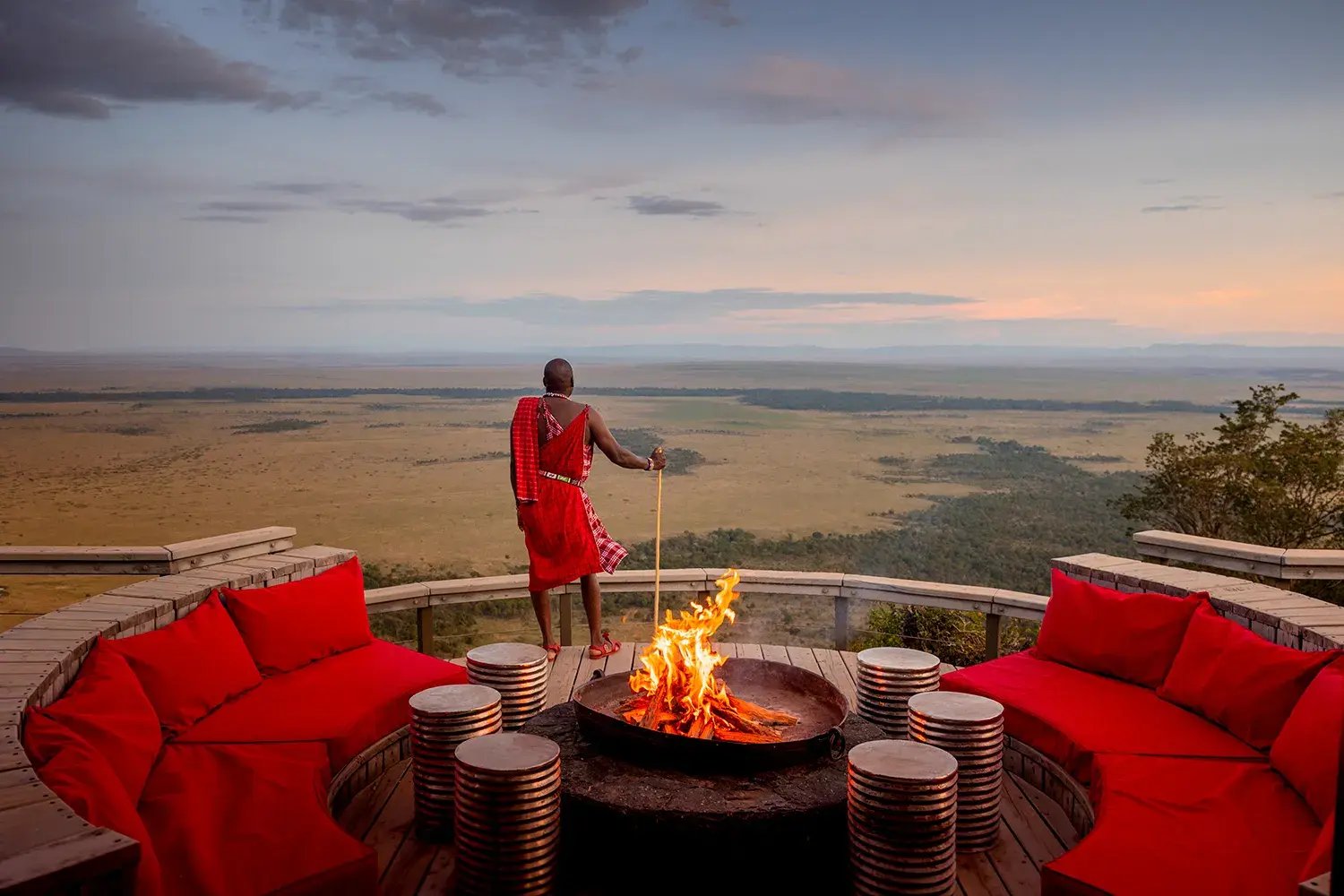 Ein Maasai blickt von einer Terrasse mit Feuerschale auf das vor ihm liegende weite Land.