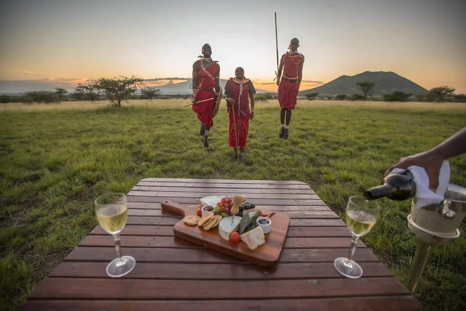 Drei Maasai-Krieger springen in die Luft, vor ihnen steht ein Tisch mit Getränken und Snacks.