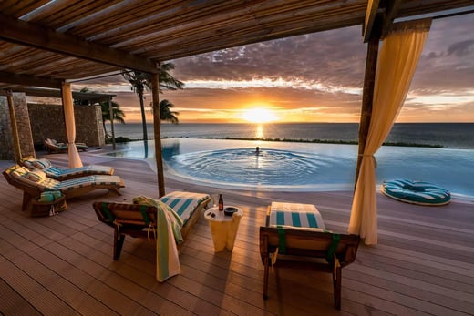 Infinitypool mit Sonnenliegen mit Blick aufs Meer bei Sonnenuntergang.