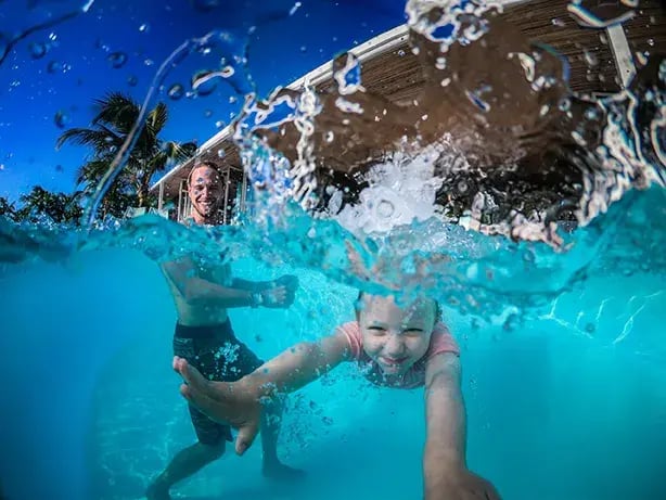 Zwei Kinder planschen im Pool, eines taucht auf die Kamera zu.