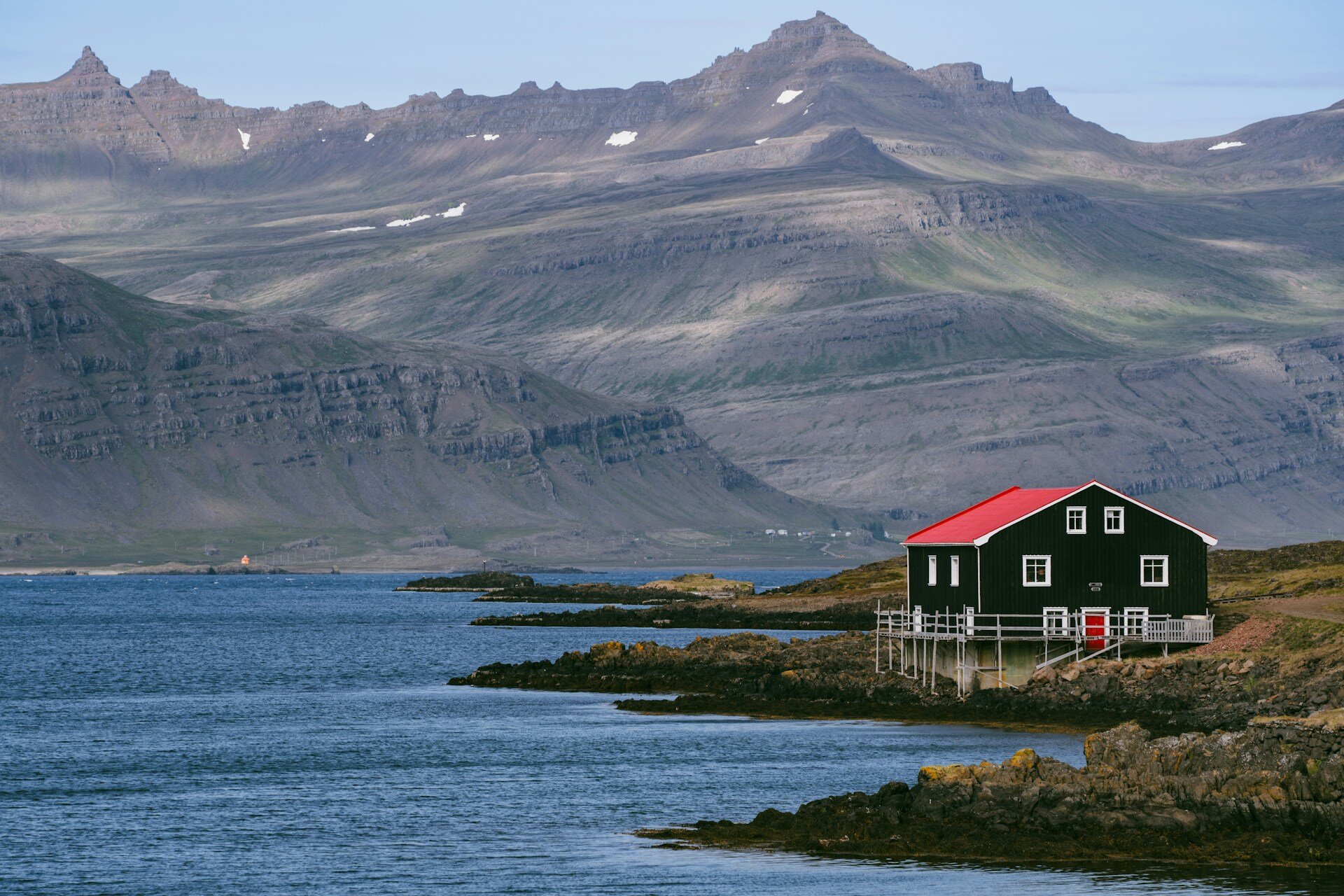 ein Haus mit rotem Dach am Meer gelegen mit Bergen im Hintergrund