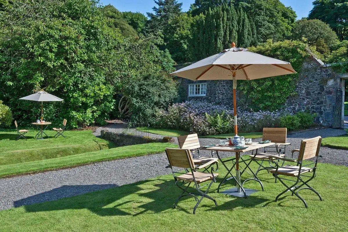 Gartenmöbel mit Sonnenschirm stehen in einer gepflegten Gartenanlage.