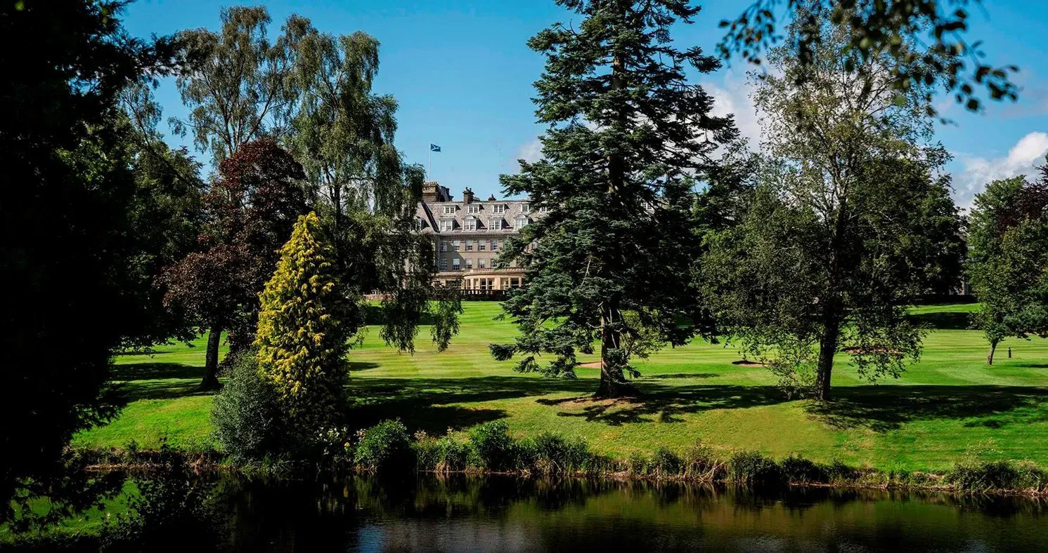 Durch einen Park mit Bäumen hindurch ist ein Schloss zu erkennen.