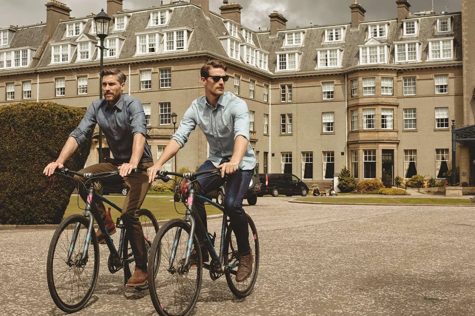 Zwei Männer fahren mit dem Fahrrad von einem Schloss weg.