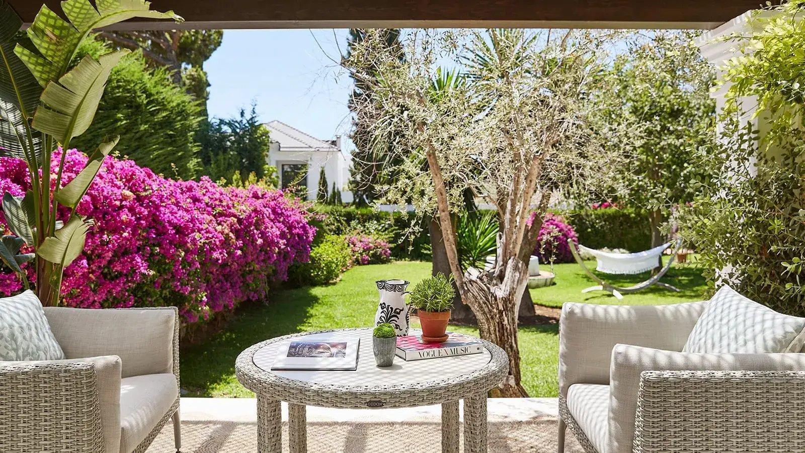 Überdachte Terrasse mit Sitzmöbeln vor einem Garten.