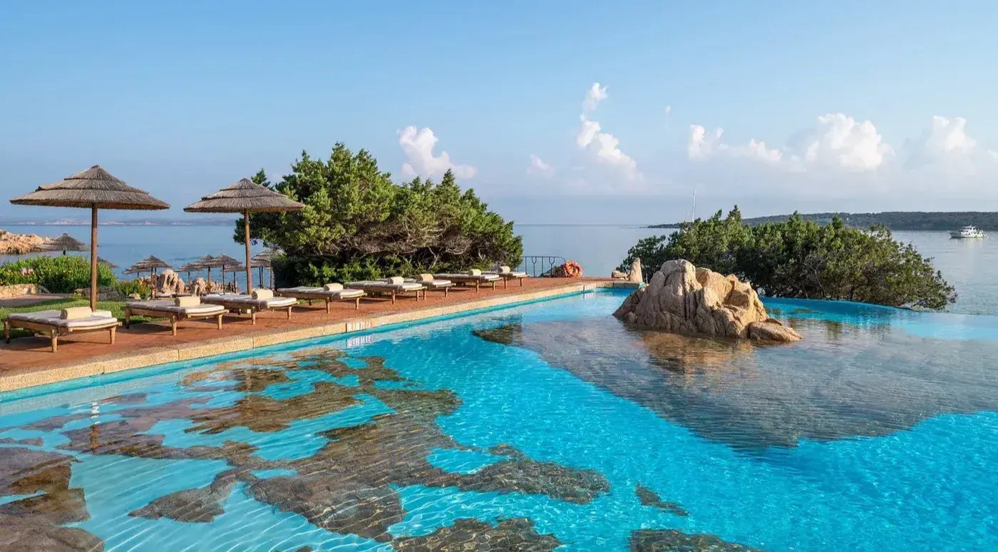 Swimmingpool mit Naturelementen, auf einem Steg sind Liegen aufgereiht.