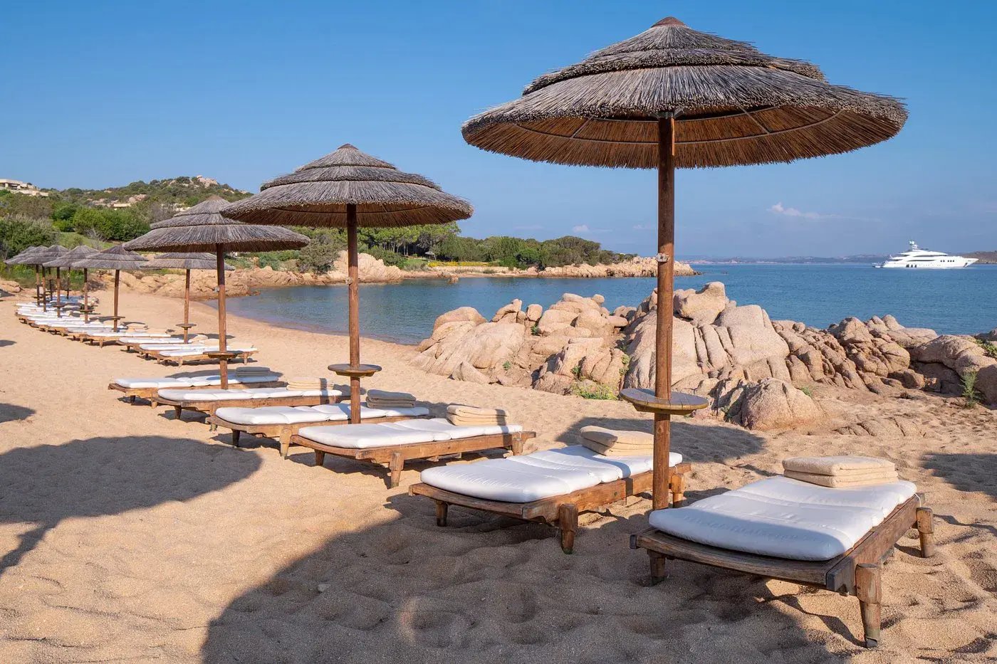 Strand mit Liegen und Schirmen mit Blick auf das Meer und einer Yacht.