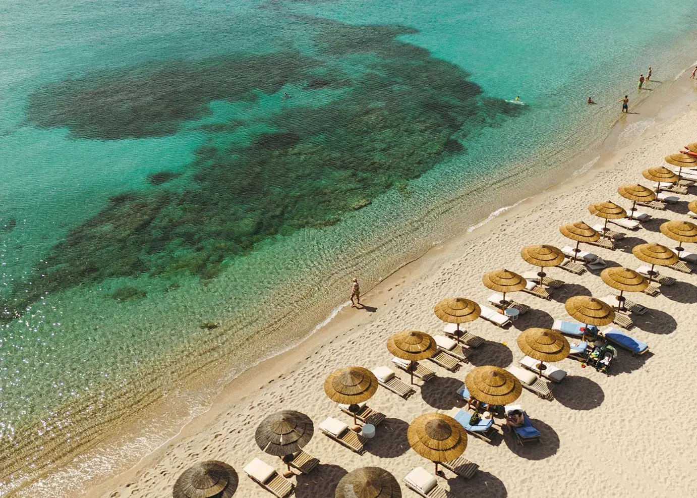 Sandstrand mit Meer, an dem viele Liegen mit Sonnenschirmen aufgereiht sind.